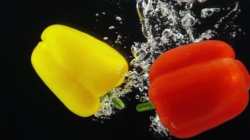 Zwei reife Paprikaschoten fallen durch Wasser