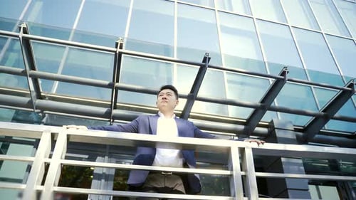 Confident young Asian businessman standing at the railing modern skyscraper office building