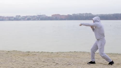 Man Shadow Boxing on a Beach near a City