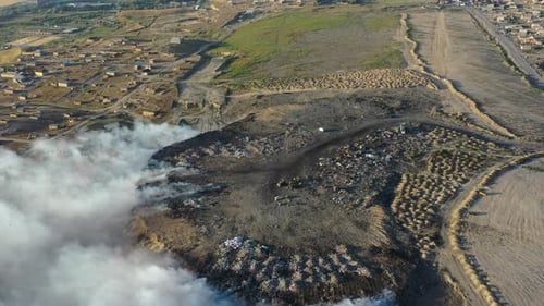 Burning garbage pile in trash landfill polluting city with smoke