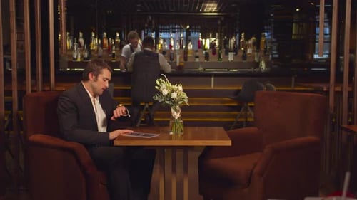 Man Sits at a Table in a Cafe, Waits and Looks at Watch