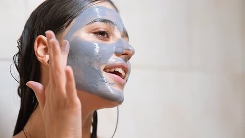 Woman Applying Gray Facial Mask in Bathroom