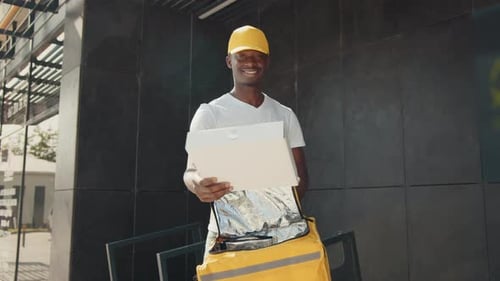 A Handsome AfricanAmerican Courier Charmingly Smiling at the Camera Pulls a