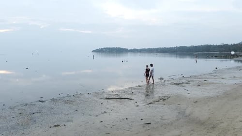 Interracial Travelers Couple Walking on Island Beach in Shallow Sea Water at Sunset Holding Hands