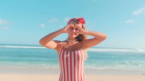 Joven mujer caucásica romántica en traje de baño mostrar corazón se encuentra en la playa del mar