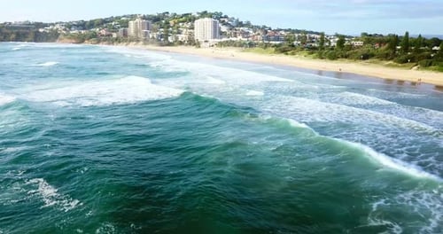 Aerial view taken by drone flying over sea waves hitting the beach.
