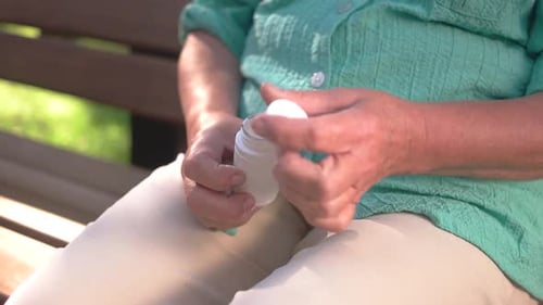 Senior Woman Opens Medicine Bottle on Park Bench