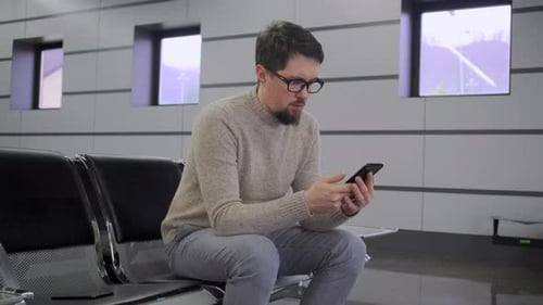 Man Using Cellphone While Sitting at Airport