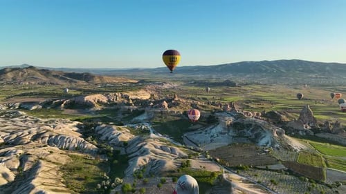 Hot air balloons fly over the mountainous landscape of Cappadocia, Turkey.