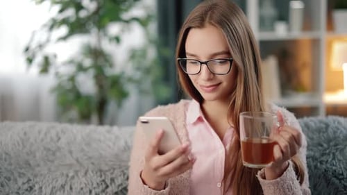 Woman Using Phone and Holding Tea Indoors