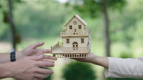 Wooden House Model Passed Between Two People