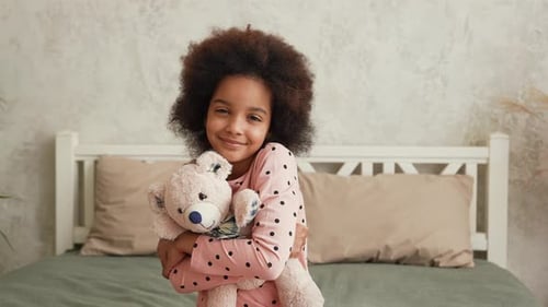 Smiling Girl Hugging Teddy Bear in Bedroom
