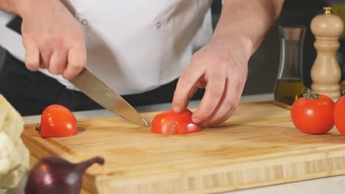 Plan rapproché d'une personne coupant une tomate avec un couteau bien aiguisé sur une planche de bois