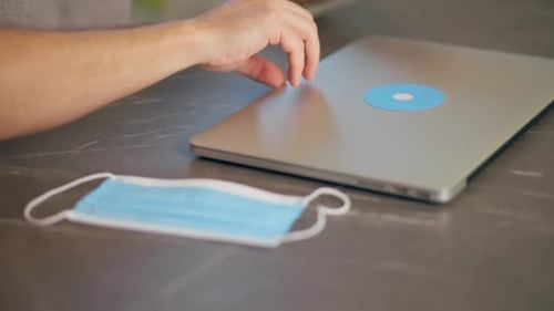 Person Typing on Laptop with Face Mask