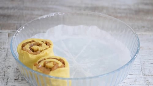 Baker put pear roll buns into glass baking form. Woman makes a yeast sweet roll buns.