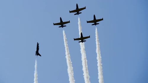 Military Jet Makes Loop Around Other Planes at Airshow, Releasing Smoke Strips.