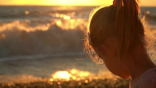 Rückansicht des Mädchens sitzt am Meer und blickt auf Wellen und Sommersonnenuntergang