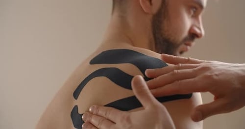 Receiving Kinesiology Tape Treatment on Shoulder Indoors