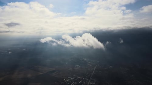 Aerial View From High Altitude of Distant City Covered with Puffy Cumulus Clouds Flying By Before
