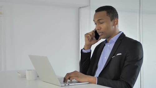 Professional Young Adult Working at Computer While Talking on Phone
