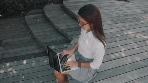 Asian Attractive Young Woman Wearing Glasses Working at Her Laptop on the Street