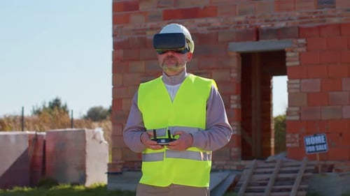 Professional Builder Drone Operator in Virtual Reality Helmet Standing in Front of Construction Site