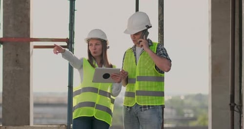 Building in Construction with a Female and a Male Builders Constructors Engineers Walking Along It