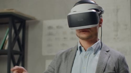 Young Man Architect in Office in Virtual Reality Helmet with Hands Commits Movements Simulating a