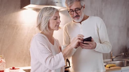 Mature Couple in Kitchen Looking at Smartphone