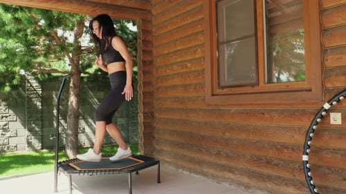 Woman Exercising on Trampoline Outside Cabin Home
