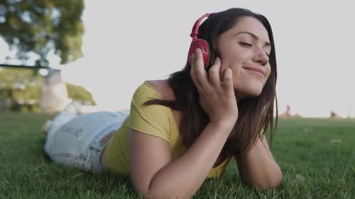 Junge hispanische Frau hört Musik mit Kopfhörern, während sie sich im Park auf grünem Gras entspannt