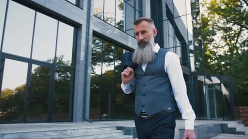 Handsome Bearded Mature Man in Suit Walking Outdoors on Modern Building Background During Sunny Day