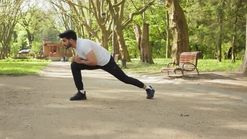 Active Male Athlete in Sport Clothes Stretching Legs Before Morning Run at Green