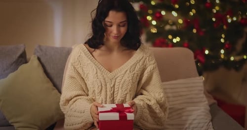 Woman Opens Christmas Gift by Tree