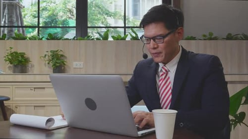 Young asian businessman is call center wearing headset talking with customer at office.