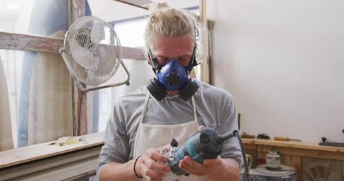 Caucasian male surfboard maker wearing a face mask and making a surfboard