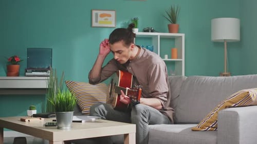 Young Adult Plays Guitar and Writes Song at Home