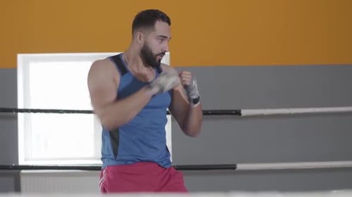 Middle Shot of Muscular Boxer Punching Air in Boxing Ring. Side View of Confident Young Middle