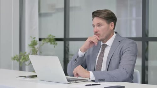 Middle Aged Man Thinking while Working on Laptop in Office