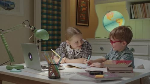 Two Kids Writing in Notebooks While Remote Learning and Online Lesson on Laptop