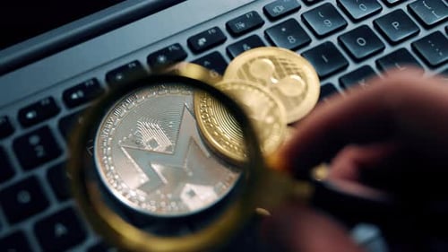 Examining Cryptocurrency Coins on Laptop Keyboard with Magnifying Glass