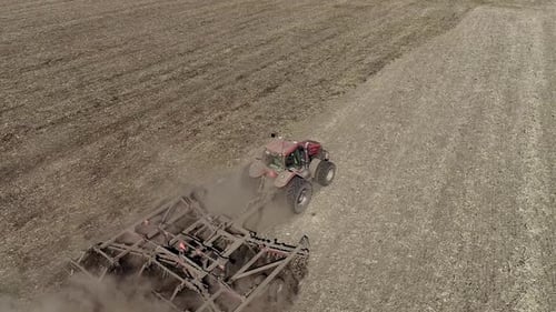 Tractor Ploughing a Field with a Trail of Dust Behind it