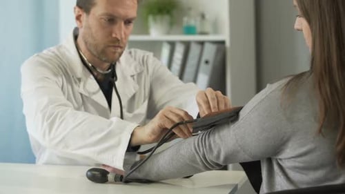 Serious Therapist Measuring the Blood Pressure of Female Patient at Clinic
