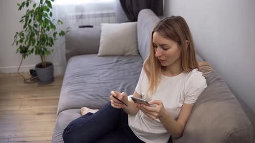 Woman Uses Phone and Credit Card on Couch