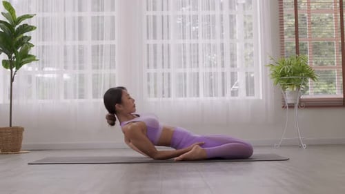 Sur un tapis de yoga, une femme asiatique suit un entraînement d'enlèvement de bridge.