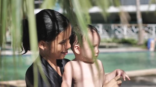 Woman Holding Baby Near Poolside in Tropics