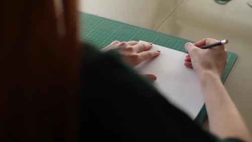 Closeup View From Back of Unrecognizable Young Woman Making Mark on White Paper Lying on Green