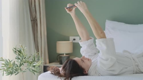 Woman in Robe Relaxing and Using Phone in Bed