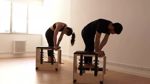 Athletes doing exercises on pilates chair in gym