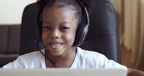 Head Shot Close-up Web Cam View of Afro Child Girl in Headphones Speaks Into Microphone, Actively